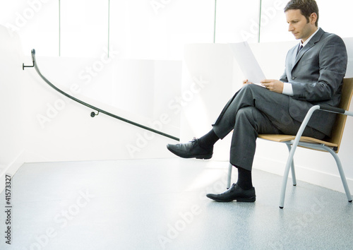 Photo: Businessman sitting on chair with legs crossed, looking at document Businessman sitting on chair with legs crossed, looking at document