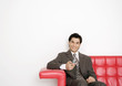 Photo : Young businessman sitting on sofa, holding cell phone, and smiling Young businessman sitting on sofa, holding cell phone, and smiling