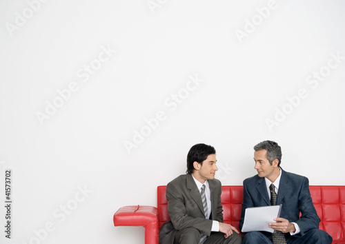 Photo: Two businessmen discussing document together on sofa Two businessmen discussing document together on sofa