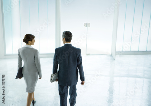 Foto: Male and female business partners walking toward door in lobby Male and female business partners walking toward door in lobby