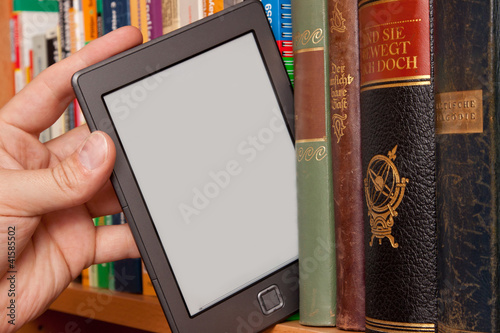 Photo: eBook vs Buch, e-Reader aus einem Bücherregal ziehen eBook vs Buch, e-Reader aus einem Bücherregal ziehen