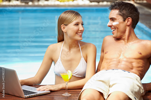 Photo: Paar mit Laptop am Pool Paar mit Laptop am Pool