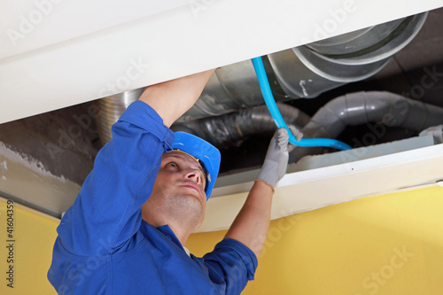 Photo: Worker holding blue pipe in place under air ducts Worker holding blue pipe in place under air ducts