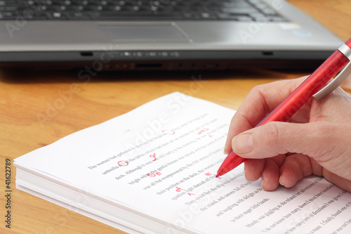 Photo: Hand with red pen proofreading by laptop Hand with red pen proofreading by laptop