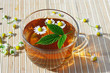 Photo: Cup of herbal tea with chamomile and green leaf still life Cup of herbal tea with chamomile and green leaf still life