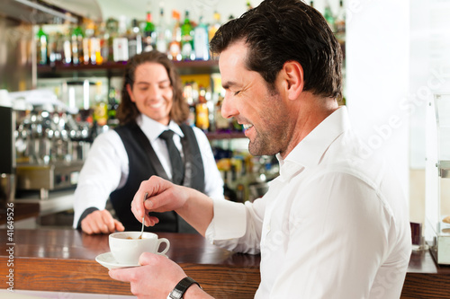Photo: Barista mit Gast in seinem Cafe oder Coffeeshop Barista mit Gast in seinem Cafe oder Coffeeshop