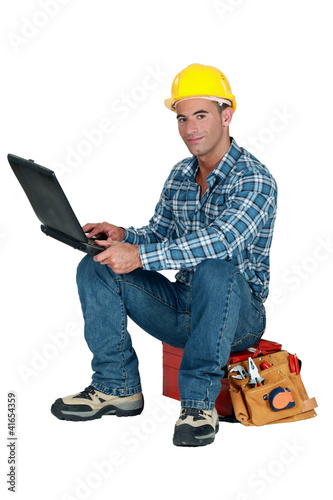 Photo: Tradesman sitting on his toolbox and using his laptop Tradesman sitting on his toolbox and using his laptop