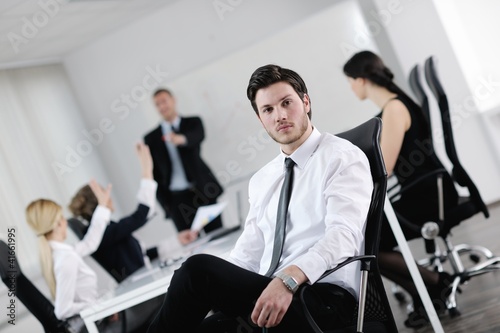 Photo: handsome young business man with colleagues in background handsome young business man with colleagues in background