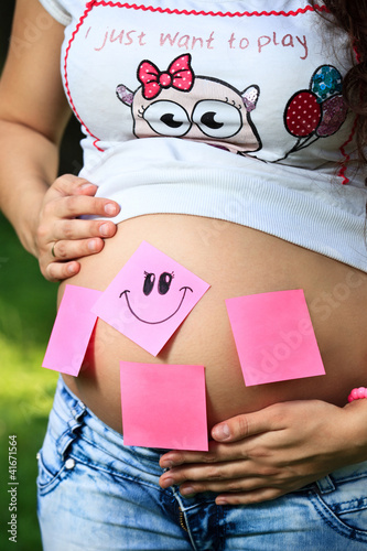 Photo: Pregnant girl with stickers on her belly holding it with both ar Pregnant girl with stickers on her belly holding it with both ar