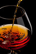 The glass with splashes cognac on black background