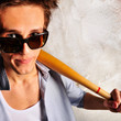 Portrait of young guy with bat leaning on the wall