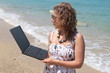 Curly hair young woman with her laptop at the beach