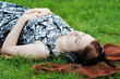 Pensive young woman lying on grass listening to music outdoors