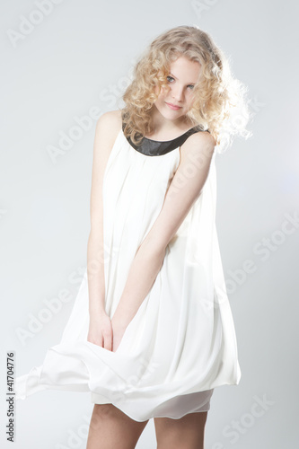 Foto: Young blonde girl posing in studio in white dress Young blonde girl posing in studio in white dress