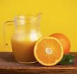 Orange juice in pitcher and oranges. Isolated on yellow Orange juice in pitcher and oranges. Isolated on yellow