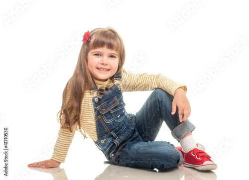 Photo: cute little girl wearing jeans overall sitting on the floor and cute little girl wearing jeans overall sitting on the floor and
