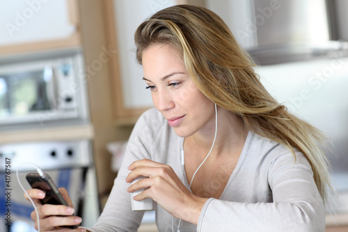 Foto: Young woman using smartphone at home with earphones Young woman using smartphone at home with earphones