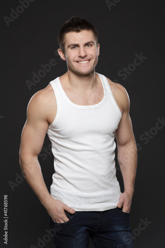 Photo: Young muscular man in white shirt posing with hands in pockets Young muscular man in white shirt posing with hands in pockets