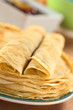 Fresh homemade crepes piled on plate with jam in the back