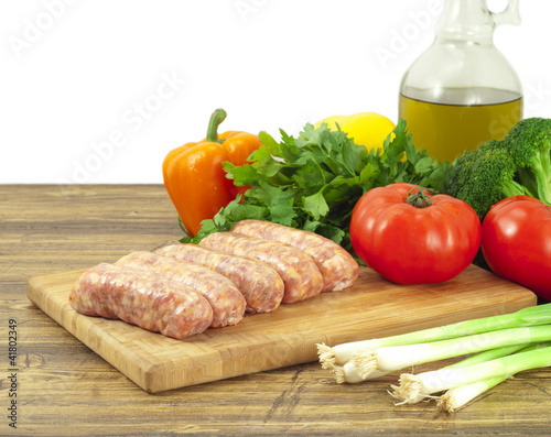 Foto: Raw sausages and fresh vegetables on a cutting board Raw sausages and fresh vegetables on a cutting board