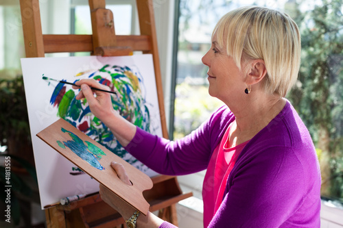 Photo: Happy elderly woman painting for fun at home Happy elderly woman painting for fun at home