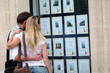 Couple looking at house-for-sale ads through shop window