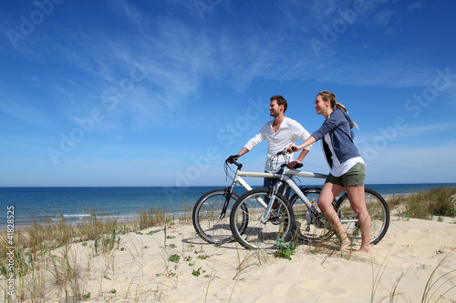 Photo: Couple standing on a sand dune with bicycles Couple standing on a sand dune with bicycles