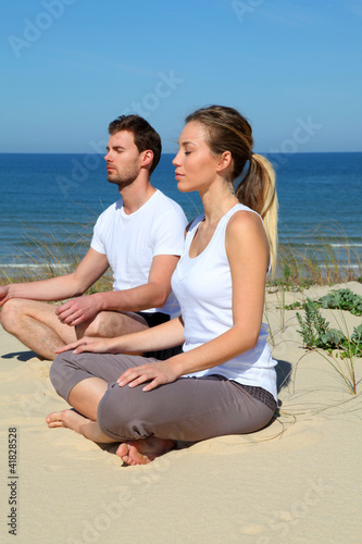 Foto: Couple doing yoga exercices on a sandy beach Couple doing yoga exercices on a sandy beach