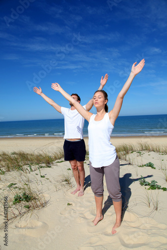 Photo: Couple meditating at the beach with arms up Couple meditating at the beach with arms up