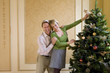 Couple indoors putting angel on top of Christmas tree, smiling, portrait.