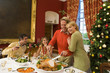 Family having Christmas dinner, woman embracing husband cutting turkey