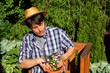 Man mit Sonnenhut in Holzstuhl pflanzt Blume
