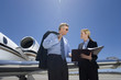 Photo: Businesswoman showing businessman in sunglasses folder by aeroplane on runway, low angle view Businesswoman showing businessman in sunglasses folder by aeroplane on runway, low angle view