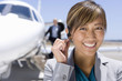 Photo: Businesswoman with hand on earpiece by man on aeroplane steps, smiling, portrait, close-up Businesswoman with hand on earpiece by man on aeroplane steps, smiling, portrait, close-up