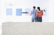 Photo: Couple holding paint roller and tray and examining blue paint samples on living room wall Couple holding paint roller and tray and examining blue paint samples on living room wall
