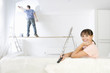 Woman smiling on sofa as man paints living room wall in background on wood plank
