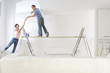Woman handing coffee cup to man painting living room wall on wood plank