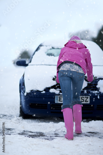 Foto: Woman pushing snow covered car in snowfall Woman pushing snow covered car in snowfall