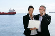 Two businesspeople stood with a laptop by the coast