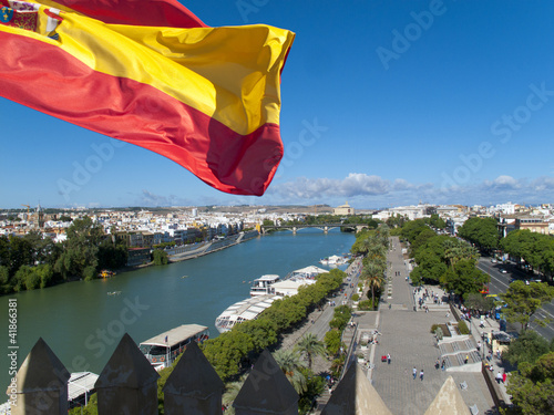 Photo: Spanish flag fluttering with city and river in background, Seville, Spain Spanish flag fluttering with city and river in background, Seville, Spain