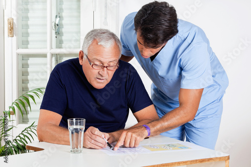 Foto: Male Nurse Helping Senior Man In Solving Puzzle Male Nurse Helping Senior Man In Solving Puzzle