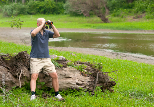 Photo: Slim bald man watching the nature through binoculars Slim bald man watching the nature through binoculars