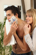 Young man shaving with his girlfriend watching