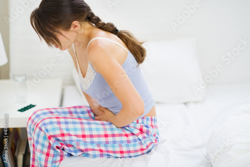 Foto: Girl with stomach ache sitting on bed Girl with stomach ache sitting on bed