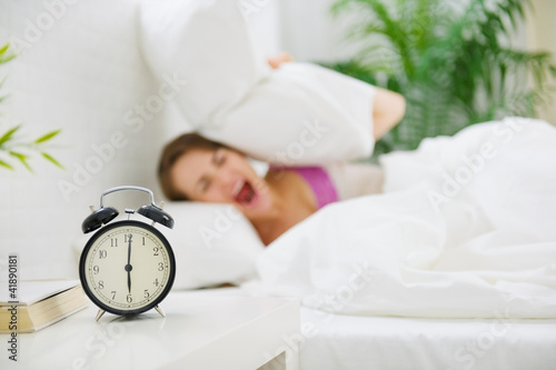 Photo: Upset woman closing ears by pillow to avoid hearing alarm clock Upset woman closing ears by pillow to avoid hearing alarm clock