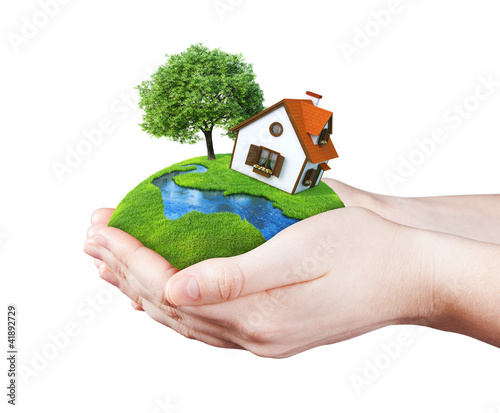 Foto: Hands holding house on clear green meadow, tree and river Hands holding house on clear green meadow, tree and river