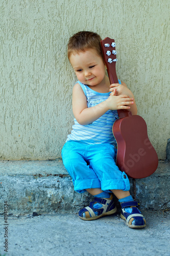 Photo: cute baby boy with guitar sitting against the concrete wall cute baby boy with guitar sitting against the concrete wall