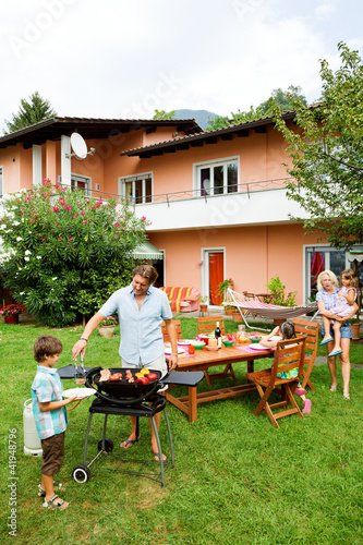 Photo: Family having a barbecue in the garden, eating Family having a barbecue in the garden, eating