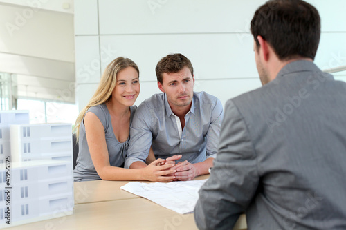 Photo: Couple in real-estate agency talking to construction planner Couple in real-estate agency talking to construction planner