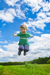 A happy boy jumps on the meadow under blue sky.